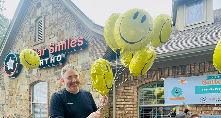 Doctor Daaboul holding smiley face balloons in front of Grapevine dental office