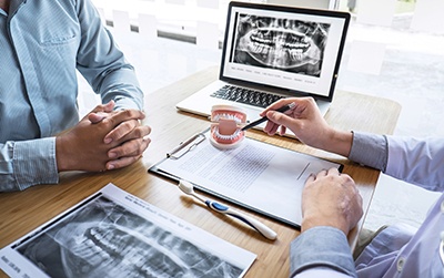 Dentist reviewing model of teeth and X-rays with patient